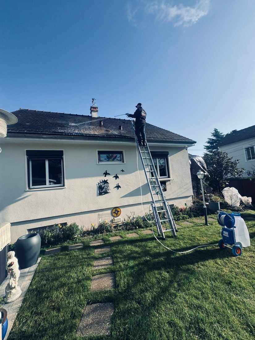 Robert Daniel, couvreur, démousse une toiture à l'échelle dans l'Essonne