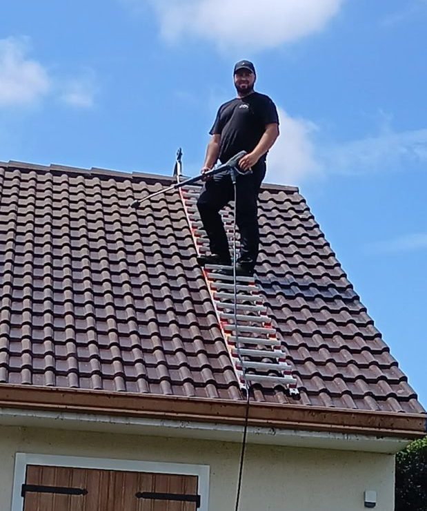 Robert Daniel, couvreur, nettoie une toiture en tuiles au nettoyeur dans l'Essonne